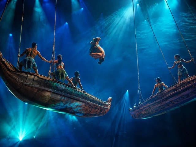 Acrobates s'élançant de balançoires en forme de pirogue de voyage sous une lumière de scène bleue