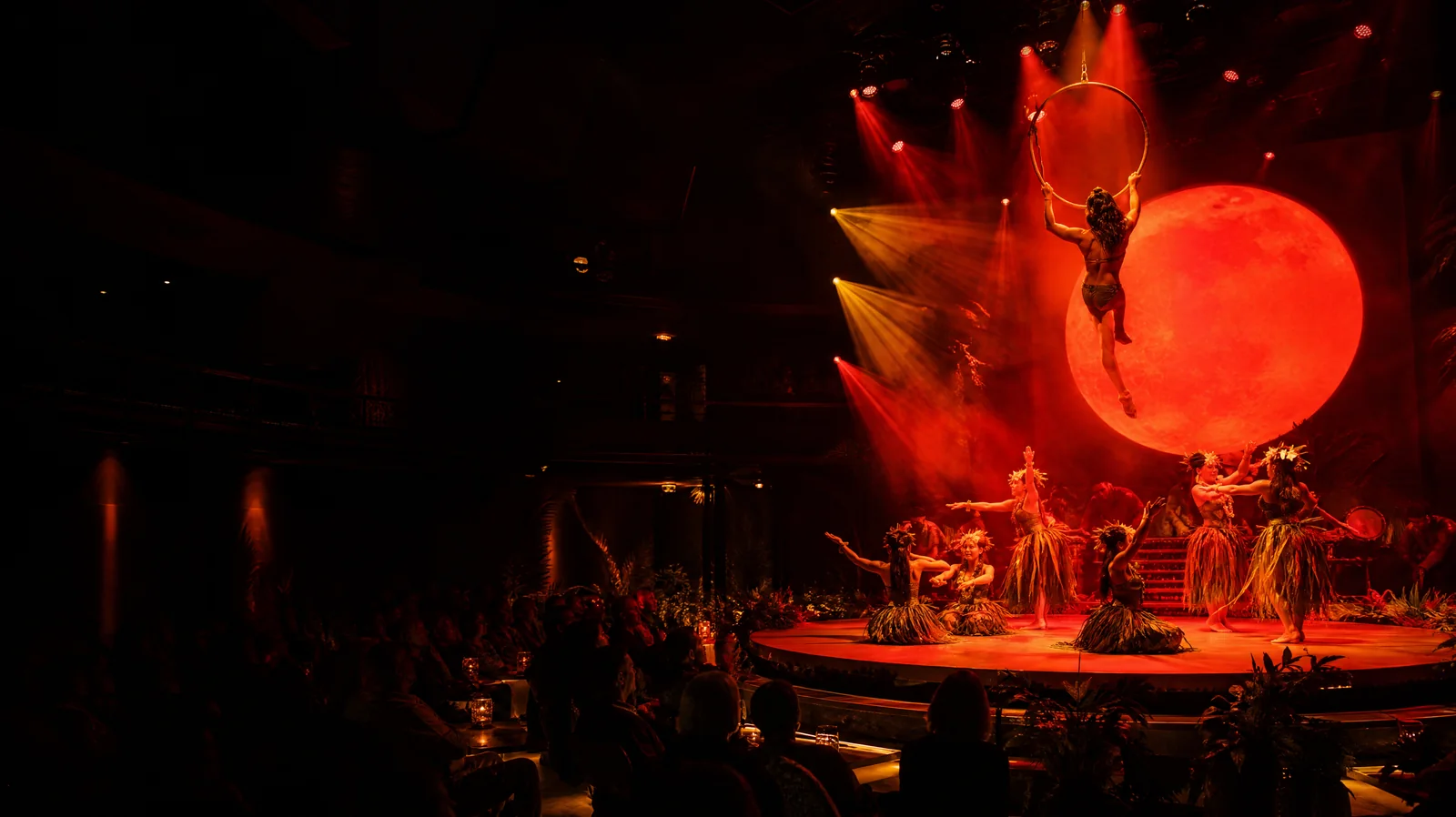 Artiste aérien sur un cerceau doré au-dessus d'une scène de cirque à thème hawaïen à Waikiki